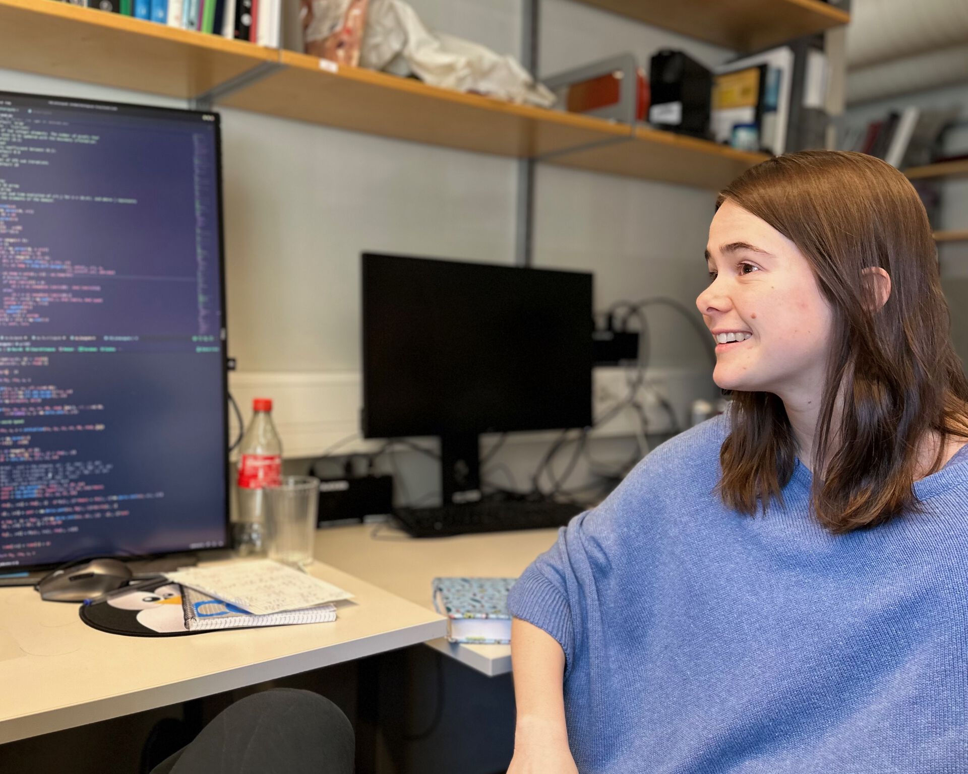 Bildet av en ung, smilende kvinne sittende foran en PC.