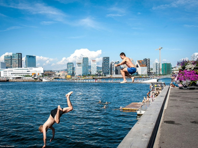 People jump into the water to bathe in the summer sun, with Oslo in the background