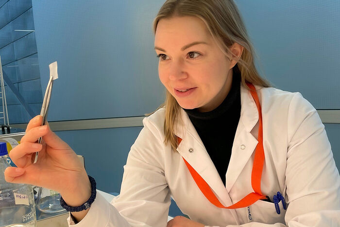 Julia Alopaeus, i laboratoriefrakk, held opp ein bit film med ein pinsett