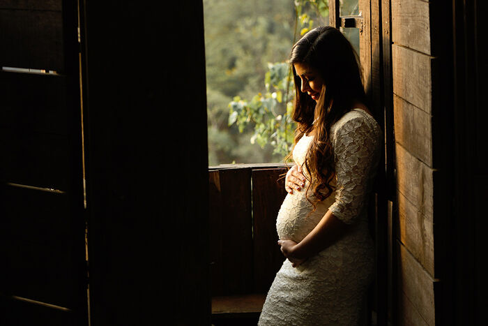 Gravid kvinne i sollys gjennom vindauga i eit elles mørkt rom