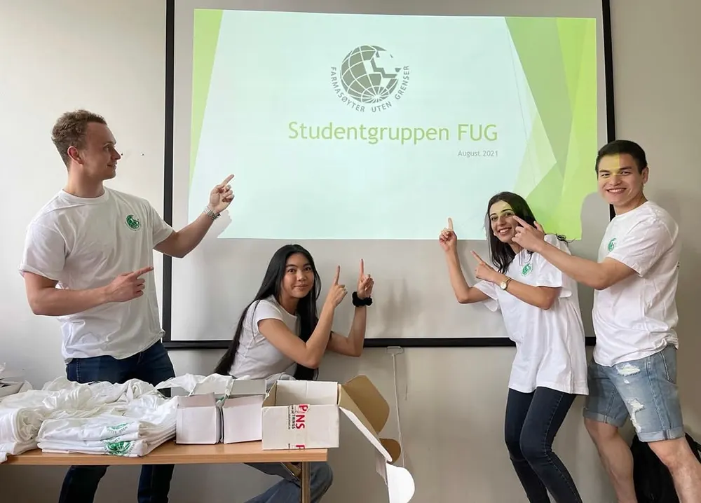 Fire studenter fra FUG som peker på FUGs logo på et lerret