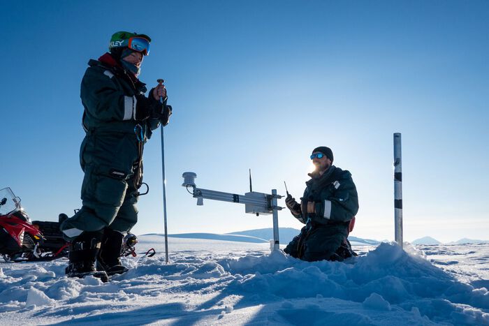 Two researchers installing a meterological station on a glacier