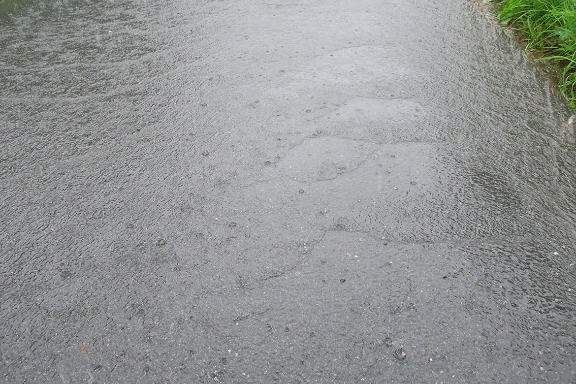 Bølger fra regnvann som renner nedover asfalt