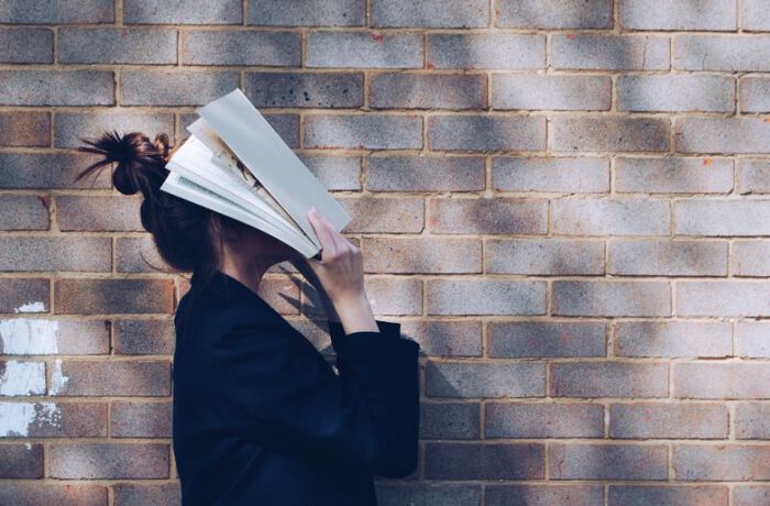 Bildet viser en person som holder en bok over ansiktet