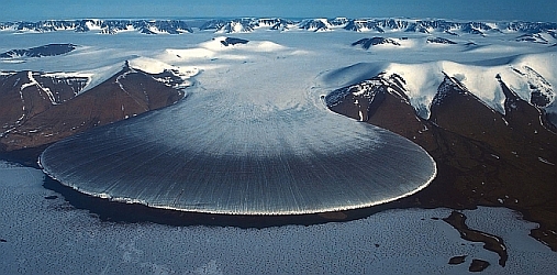 A glacier flowing out from a mountain range.